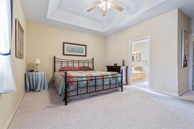 bedroom with a raised ceiling, ceiling fan, light colored carpet, and ensuite bath