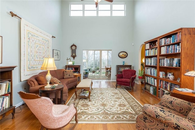 living room featuring ceiling fan, light wood-type flooring, and a towering ceiling