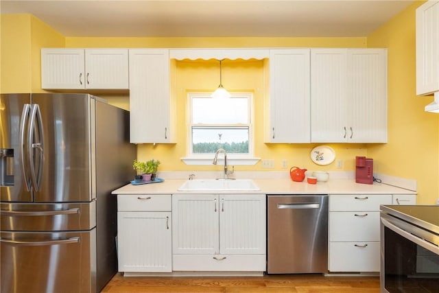 kitchen with stainless steel appliances, sink, white cabinets, light hardwood / wood-style floors, and hanging light fixtures