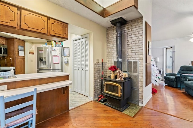 kitchen with a wood stove, ceiling fan, a textured ceiling, appliances with stainless steel finishes, and light wood-type flooring