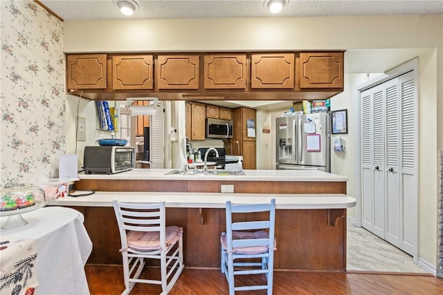 kitchen featuring kitchen peninsula, appliances with stainless steel finishes, sink, light hardwood / wood-style flooring, and a breakfast bar area