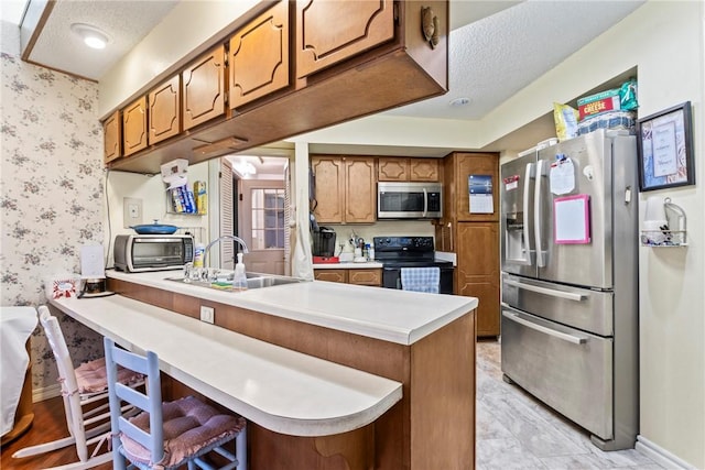 kitchen featuring kitchen peninsula, appliances with stainless steel finishes, a textured ceiling, sink, and a breakfast bar area