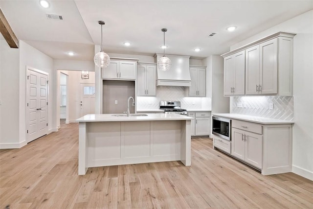 kitchen with built in microwave, hanging light fixtures, stainless steel gas range, backsplash, and custom range hood