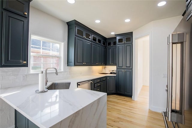 kitchen featuring light stone countertops, sink, backsplash, kitchen peninsula, and light wood-type flooring