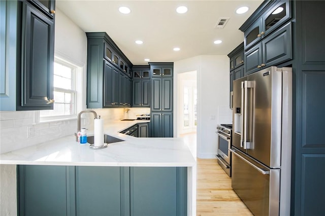 kitchen featuring sink, premium appliances, kitchen peninsula, light hardwood / wood-style floors, and decorative backsplash