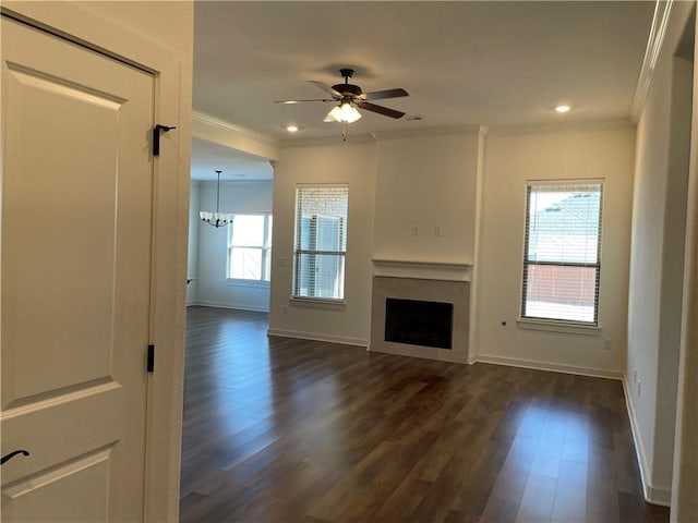 unfurnished living room featuring plenty of natural light, dark hardwood / wood-style flooring, ornamental molding, and ceiling fan with notable chandelier