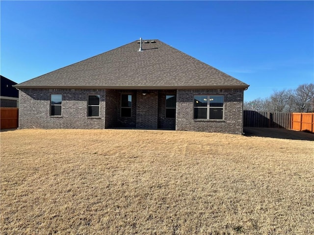 back of property featuring roof with shingles, brick siding, and a lawn