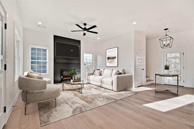 living room featuring a large fireplace, light hardwood / wood-style floors, and ceiling fan with notable chandelier