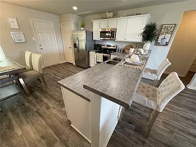 kitchen with kitchen peninsula, a kitchen breakfast bar, stainless steel appliances, dark wood-type flooring, and white cabinetry