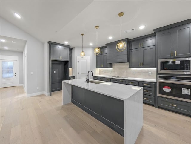 kitchen with pendant lighting, sink, appliances with stainless steel finishes, a kitchen island with sink, and light stone countertops