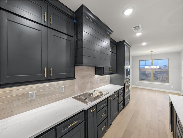 kitchen with pendant lighting, appliances with stainless steel finishes, light stone countertops, decorative backsplash, and light wood-type flooring