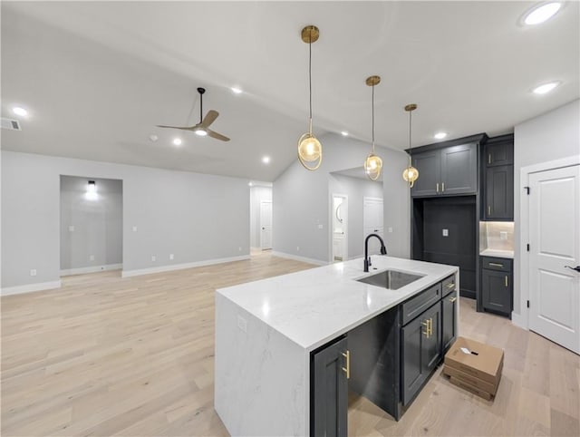 kitchen featuring light stone counters, a kitchen island with sink, sink, and hanging light fixtures