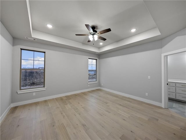 spare room featuring light hardwood / wood-style flooring, ceiling fan, and a tray ceiling