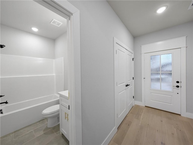 interior space with vanity, hardwood / wood-style floors, shower / washtub combination, and toilet