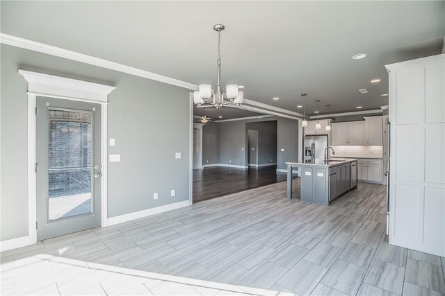 kitchen featuring ornamental molding, a breakfast bar, a kitchen island with sink, sink, and pendant lighting