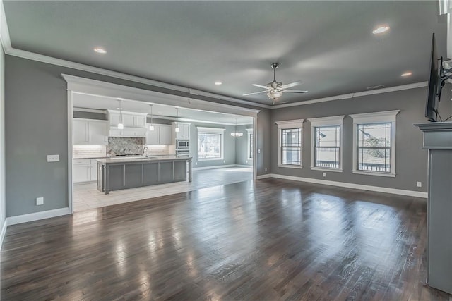 unfurnished living room featuring dark hardwood / wood-style floors, a healthy amount of sunlight, ornamental molding, and ceiling fan with notable chandelier