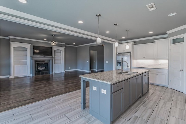 kitchen with a kitchen island with sink, white cabinets, hanging light fixtures, stainless steel fridge, and light stone countertops