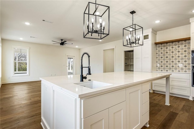 kitchen featuring visible vents, dark wood finished floors, white cabinets, hanging light fixtures, and a sink