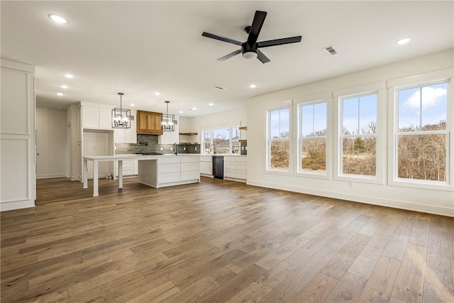 unfurnished living room with visible vents, dark wood-style floors, ceiling fan with notable chandelier, a sink, and recessed lighting