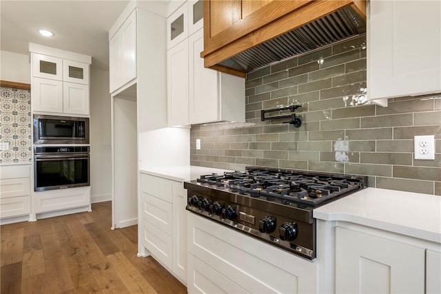 kitchen with white cabinets, custom range hood, glass insert cabinets, appliances with stainless steel finishes, and light countertops