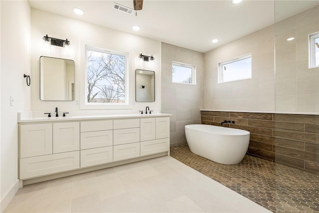 bathroom with double vanity, a sink, visible vents, and tile walls