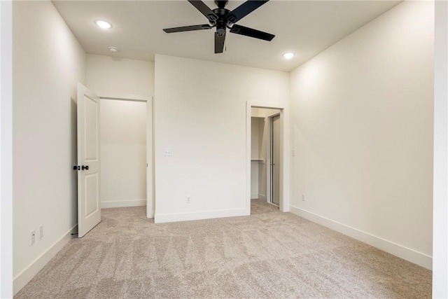 unfurnished bedroom featuring a walk in closet, light colored carpet, baseboards, and recessed lighting