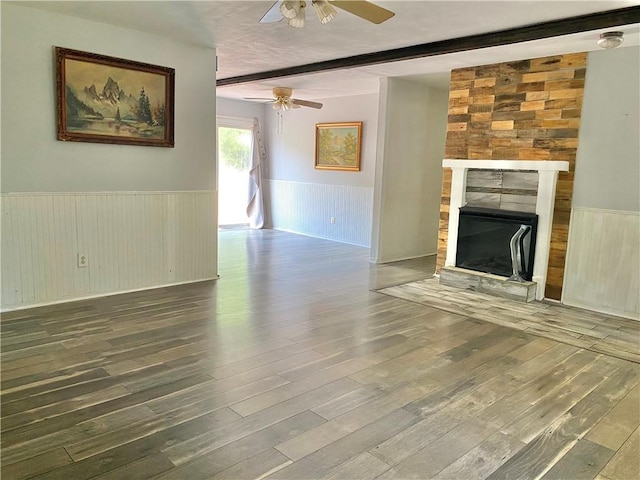 unfurnished living room featuring beam ceiling, a tile fireplace, ceiling fan, wooden walls, and hardwood / wood-style flooring