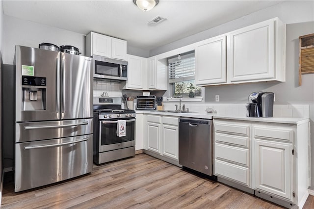 kitchen featuring stainless steel appliances, light hardwood / wood-style floors, sink, and white cabinets