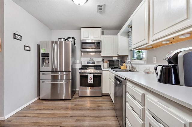 kitchen with appliances with stainless steel finishes, white cabinetry, wood-type flooring, sink, and a textured ceiling