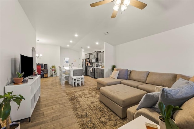 living room with sink, ceiling fan with notable chandelier, light hardwood / wood-style floors, and vaulted ceiling