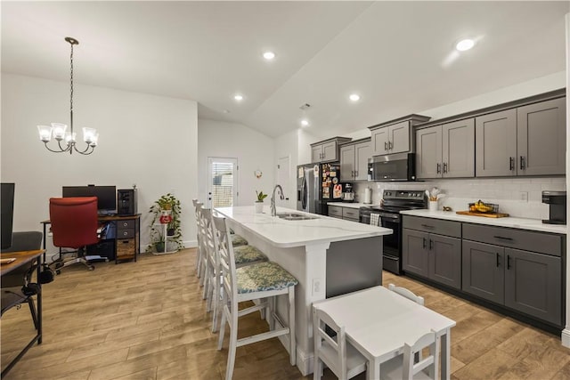 kitchen with sink, vaulted ceiling, a kitchen island with sink, appliances with stainless steel finishes, and light wood-type flooring