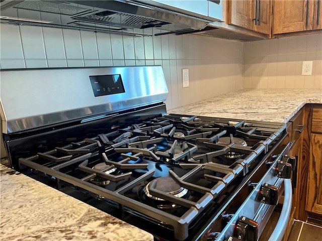 details featuring decorative backsplash, exhaust hood, light stone counters, and black range with gas cooktop