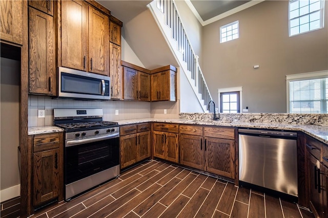 kitchen featuring tasteful backsplash, light stone counters, stainless steel appliances, sink, and a high ceiling