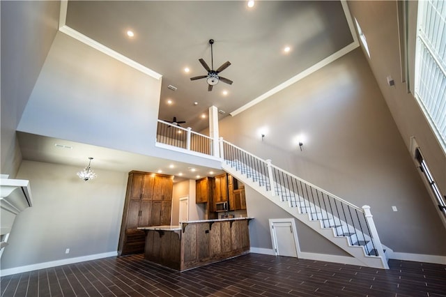 kitchen featuring a breakfast bar, a high ceiling, ceiling fan with notable chandelier, ornamental molding, and kitchen peninsula