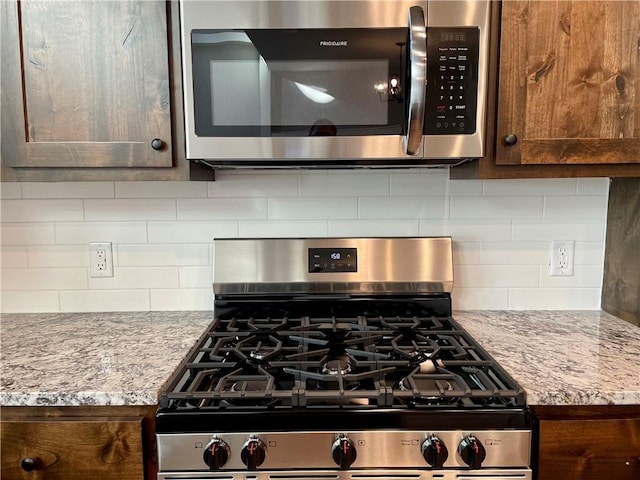 kitchen featuring light stone countertops, dark brown cabinets, backsplash, and stainless steel appliances