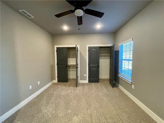 unfurnished bedroom featuring carpet, ceiling fan, and two closets