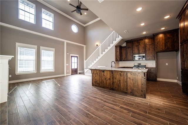 kitchen featuring ceiling fan, dark wood-type flooring, crown molding, a center island with sink, and appliances with stainless steel finishes