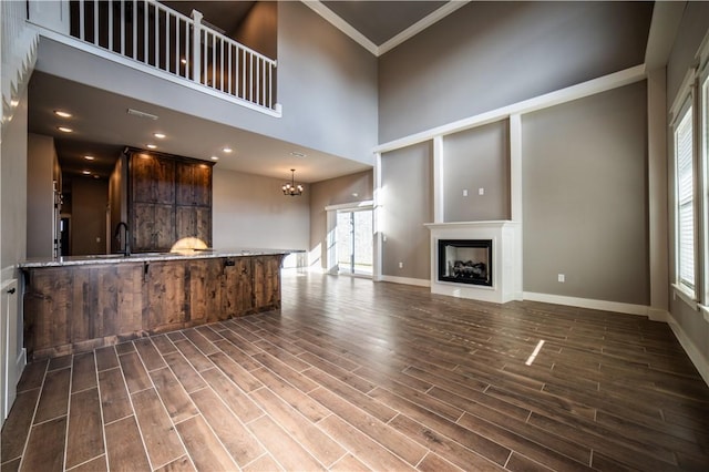 unfurnished living room featuring crown molding, sink, a towering ceiling, and a chandelier