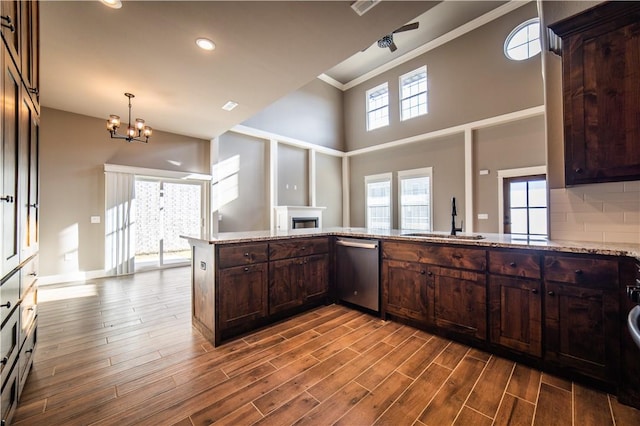 kitchen with kitchen peninsula, dark brown cabinets, sink, dishwasher, and a chandelier