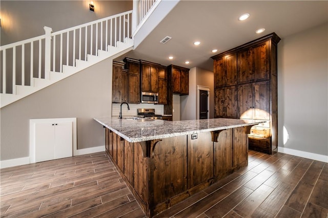 kitchen featuring a breakfast bar, dark hardwood / wood-style floors, light stone countertops, kitchen peninsula, and stainless steel appliances