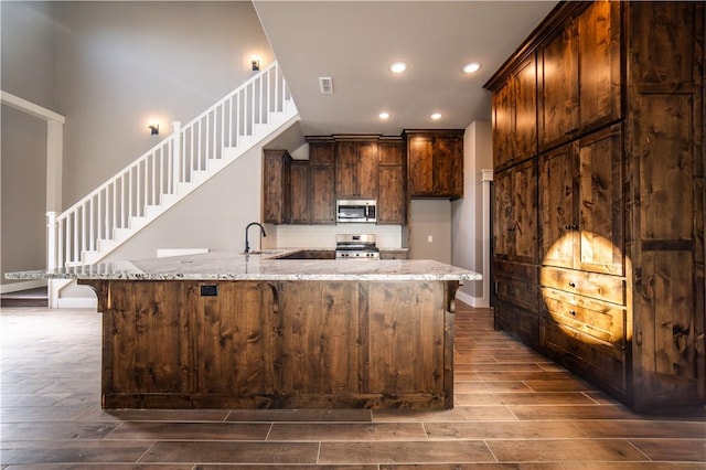 kitchen with light stone countertops, sink, kitchen peninsula, a breakfast bar, and appliances with stainless steel finishes