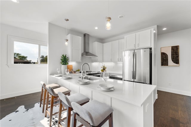 kitchen with white cabinets, stainless steel fridge, dark wood-type flooring, and wall chimney range hood