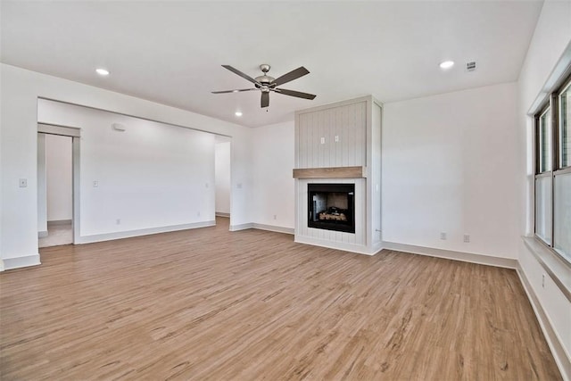 unfurnished living room featuring a large fireplace, ceiling fan, and light hardwood / wood-style floors