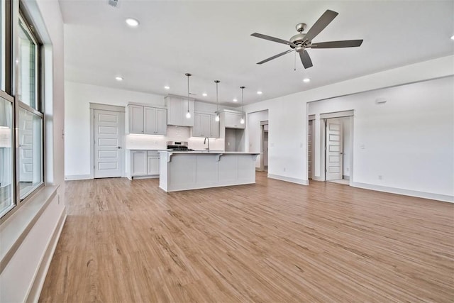 kitchen with ceiling fan, sink, pendant lighting, light hardwood / wood-style flooring, and an island with sink