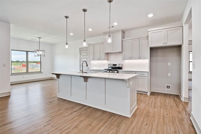 kitchen with stainless steel range, sink, pendant lighting, a kitchen island with sink, and light wood-type flooring