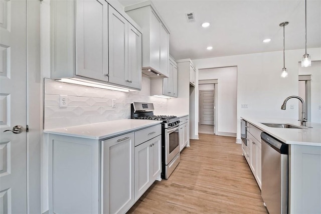 kitchen featuring pendant lighting, sink, appliances with stainless steel finishes, light hardwood / wood-style floors, and white cabinetry