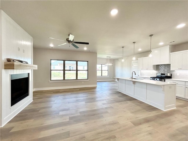 kitchen featuring gas stove, white cabinetry, sink, light hardwood / wood-style flooring, and an island with sink