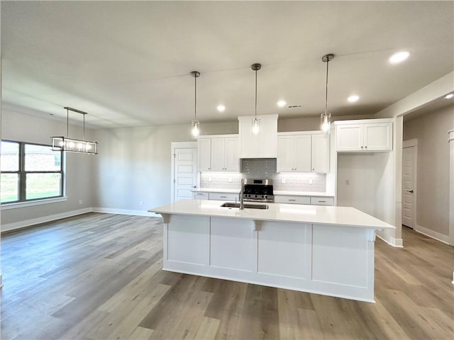 kitchen with pendant lighting, light hardwood / wood-style floors, white cabinetry, and an island with sink