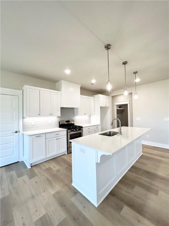 kitchen featuring sink, an island with sink, decorative light fixtures, gas stove, and white cabinetry