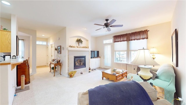 living room featuring a tiled fireplace, ceiling fan, and light colored carpet